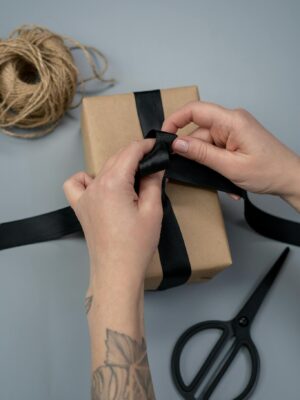 Close-up of hands tying a black ribbon around a gift box on a minimalist background.