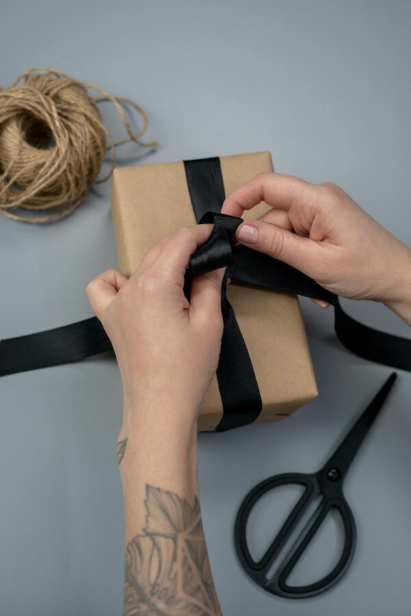 Close-up of hands tying a black ribbon around a gift box on a minimalist background.