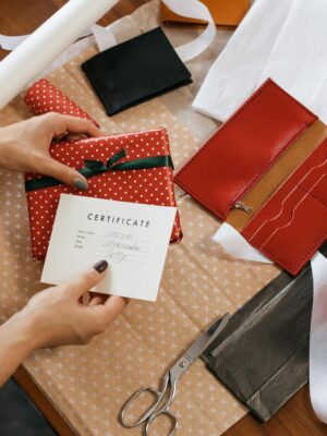 Hands wrapping gifts with a certificate on a wooden table.