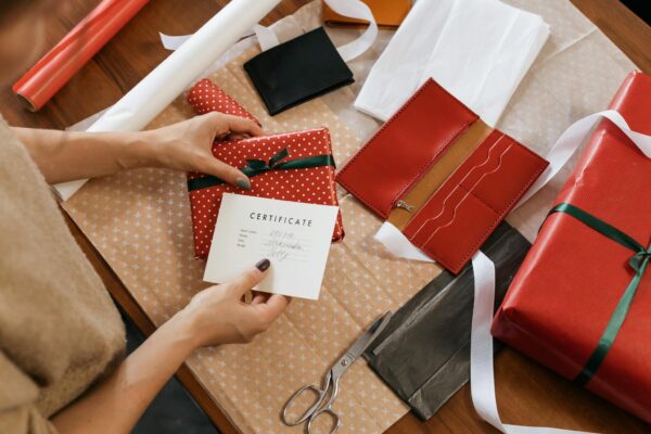 Hands wrapping gifts with a certificate on a wooden table.