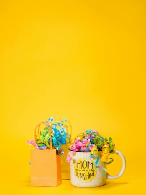 Vibrant Mother's Day gift setup with a mug and gift bags on a yellow backdrop.