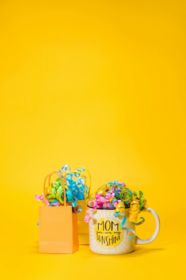 Vibrant Mother's Day gift setup with a mug and gift bags on a yellow backdrop.